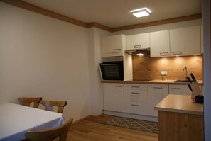 A compact kitchen with white cabinets, a built-in oven, and a wooden countertop. - Ferienwohnung 2 1 - Gästehaus Obererlacher (Obertilliach)