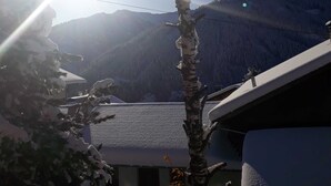 Helderblauwe lucht met de zon, een met sneeuw bedekte berg op de achtergrond, en een gebouw met een schuin dak.