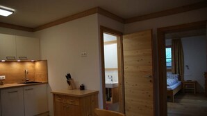 Een kamer met een bed, een houten deur, een kleine tafel en een kitchenette.