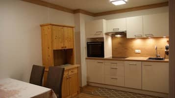 Eine kleine Küche mit Holzschränken, einem Einbauofen und einem Essbereich mit Tisch und Stühlen.