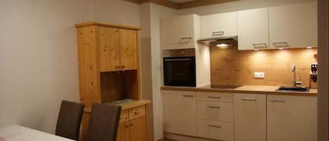 Una cocina compacta con armarios de madera, horno empotrado y comedor con mesa y sillas.