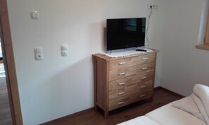 Une pièce avec une commode en bois, un téléviseur posé dessus, un canapé blanc et un plancher en bois.