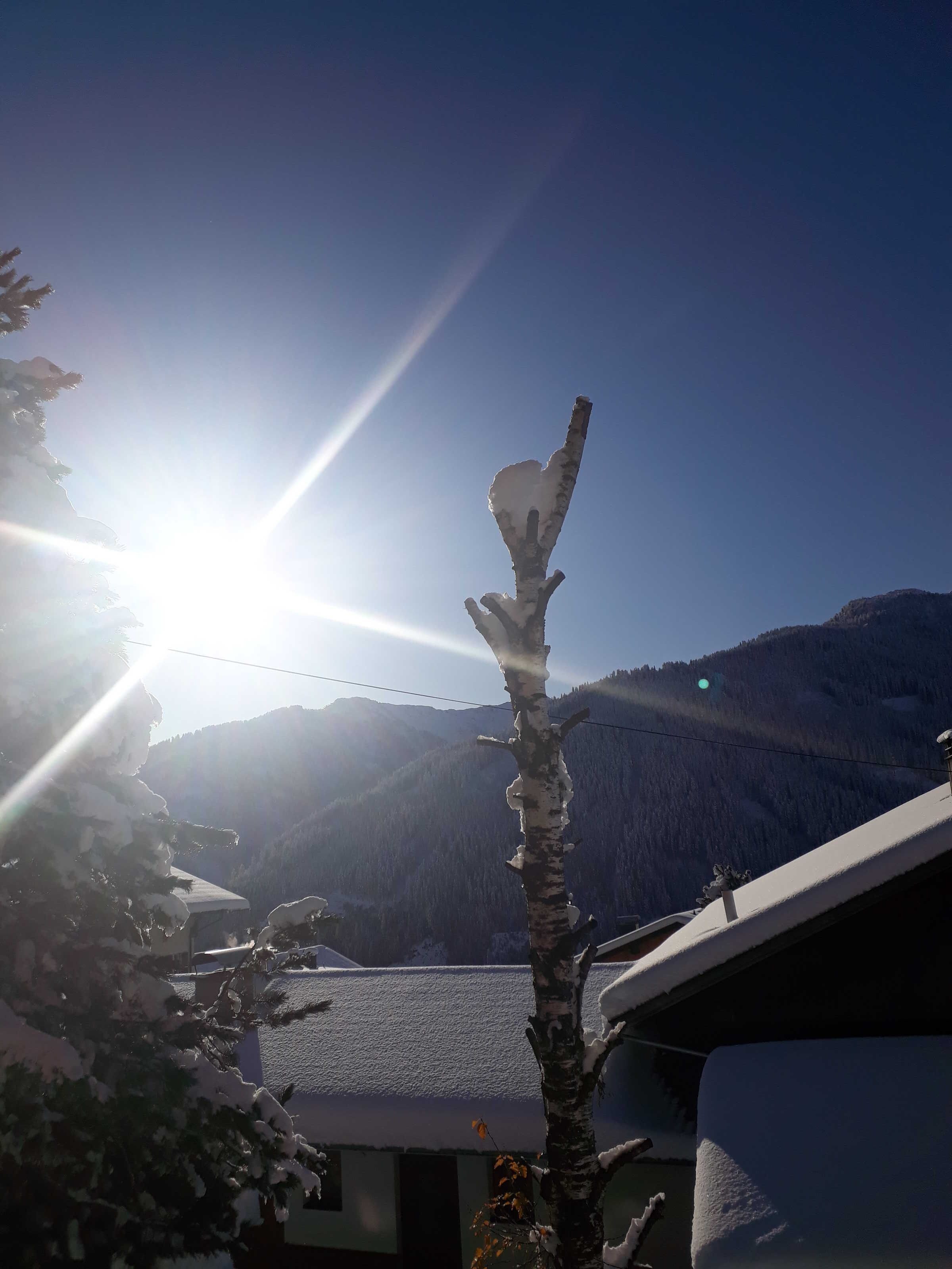 A clear sky with the sun shining, a snow-covered mountain in the background, and a building with a sloped roof.