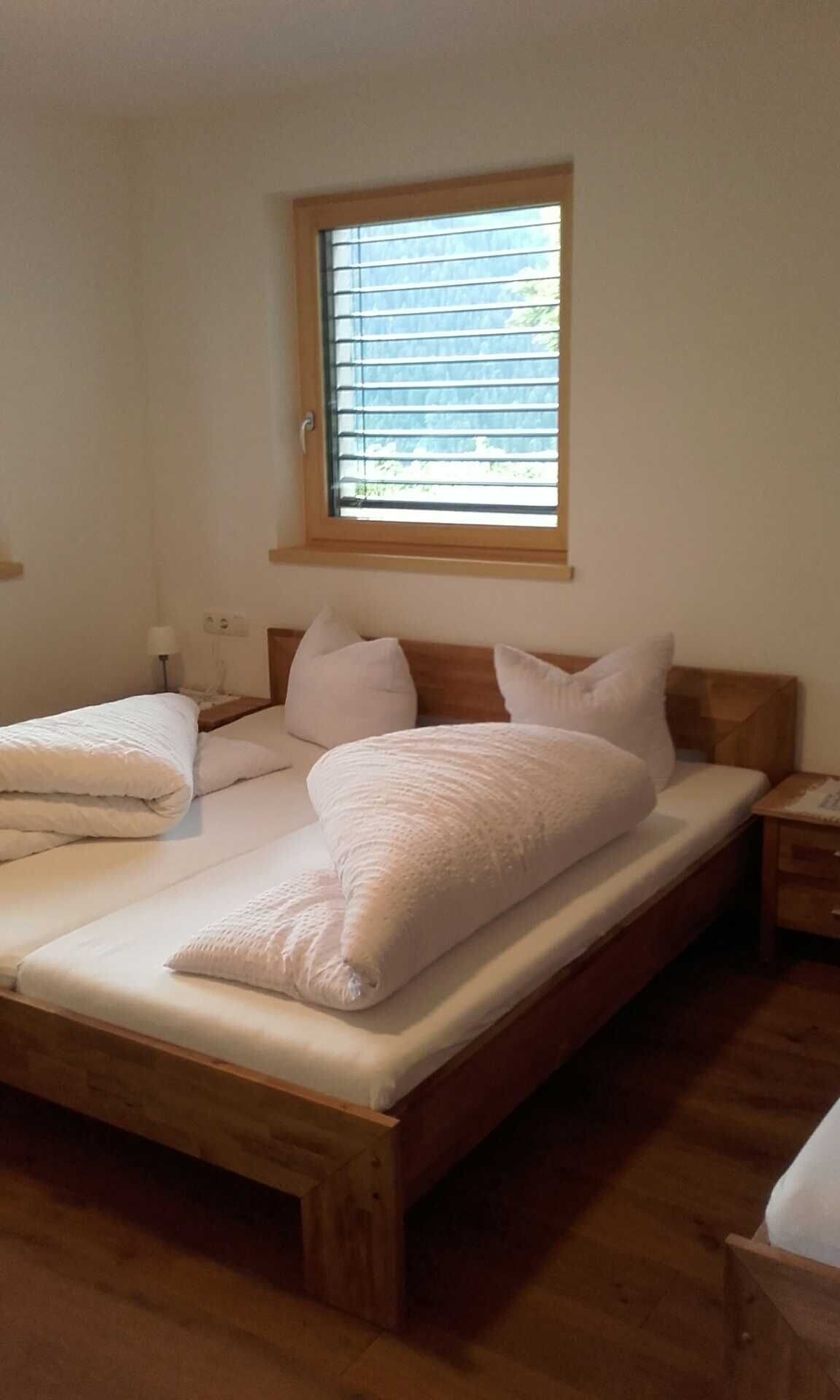A single bed with a wooden frame, a window with blinds, and a bedside table with a lamp.