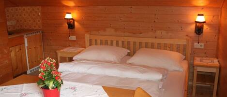 Une pièce de style cabane en bois, comprenant deux lits, une table, une chaise et deux lampes fixées au mur.