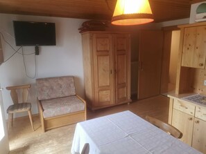 A room with a bed, a wooden cabinet, a television mounted on the wall, and a sofa.