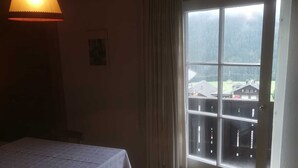 Una habitación con una mesa, una lámpara colgante, una ventana con vistas a edificios y una puerta.