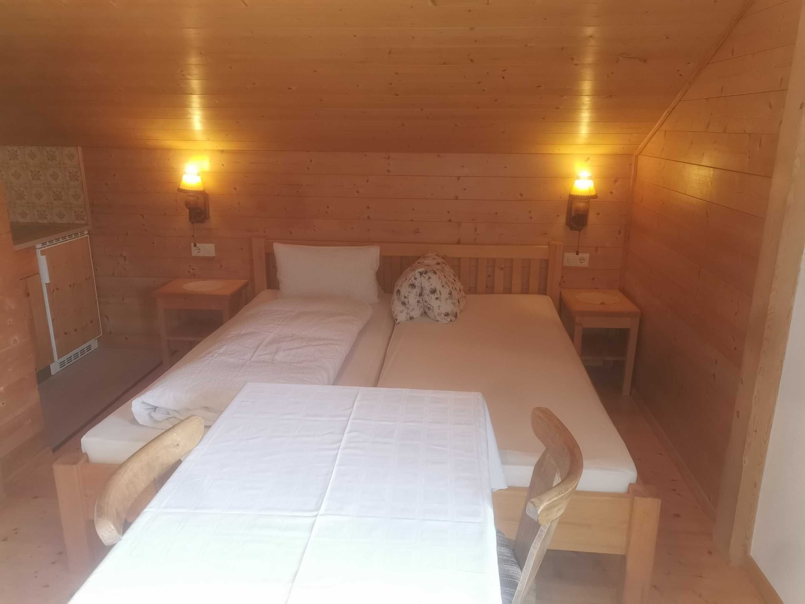 Una habitación tipo cabaña de madera con dos camas, una mesa, sillas y dos lámparas fijadas a la pared.