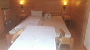 Una habitación tipo cabaña de madera con dos camas, una mesa, sillas y dos lámparas fijadas a la pared.