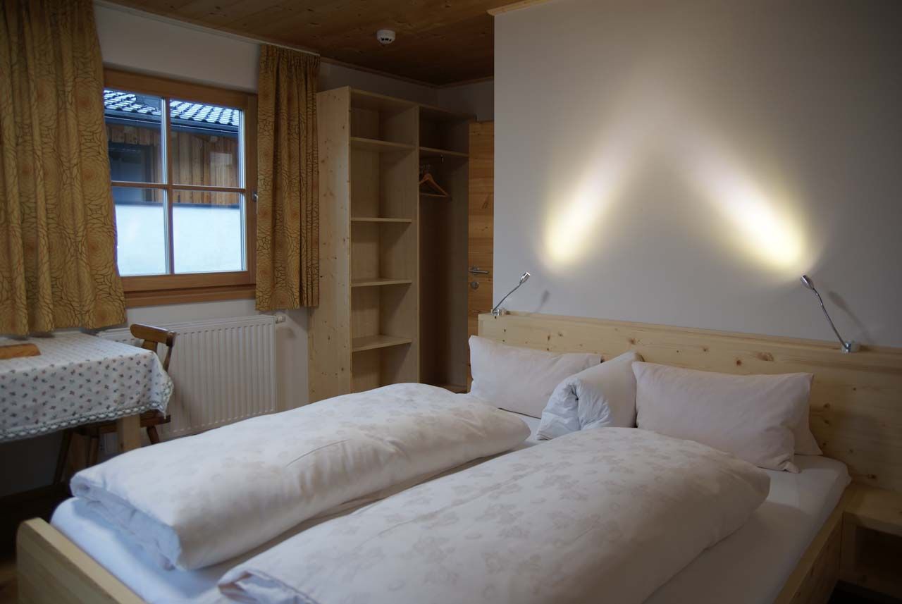 A bedroom with two beds, a wooden headboard, a bedside table, a radiator, and a window with curtains.