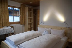 A bedroom with two beds, a wooden headboard, a bedside table, a radiator, and a window with curtains. - Ferienwohnung 4 1 - Gästehaus Obererlacher (Obertilliach)