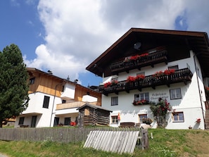 A traditional chalet-style building with a wooden facade, balconies with red flowers, and a sign indicating it is a guesthouse. - Ferienwohnung 4 1 - Gästehaus Obererlacher (Obertilliach)