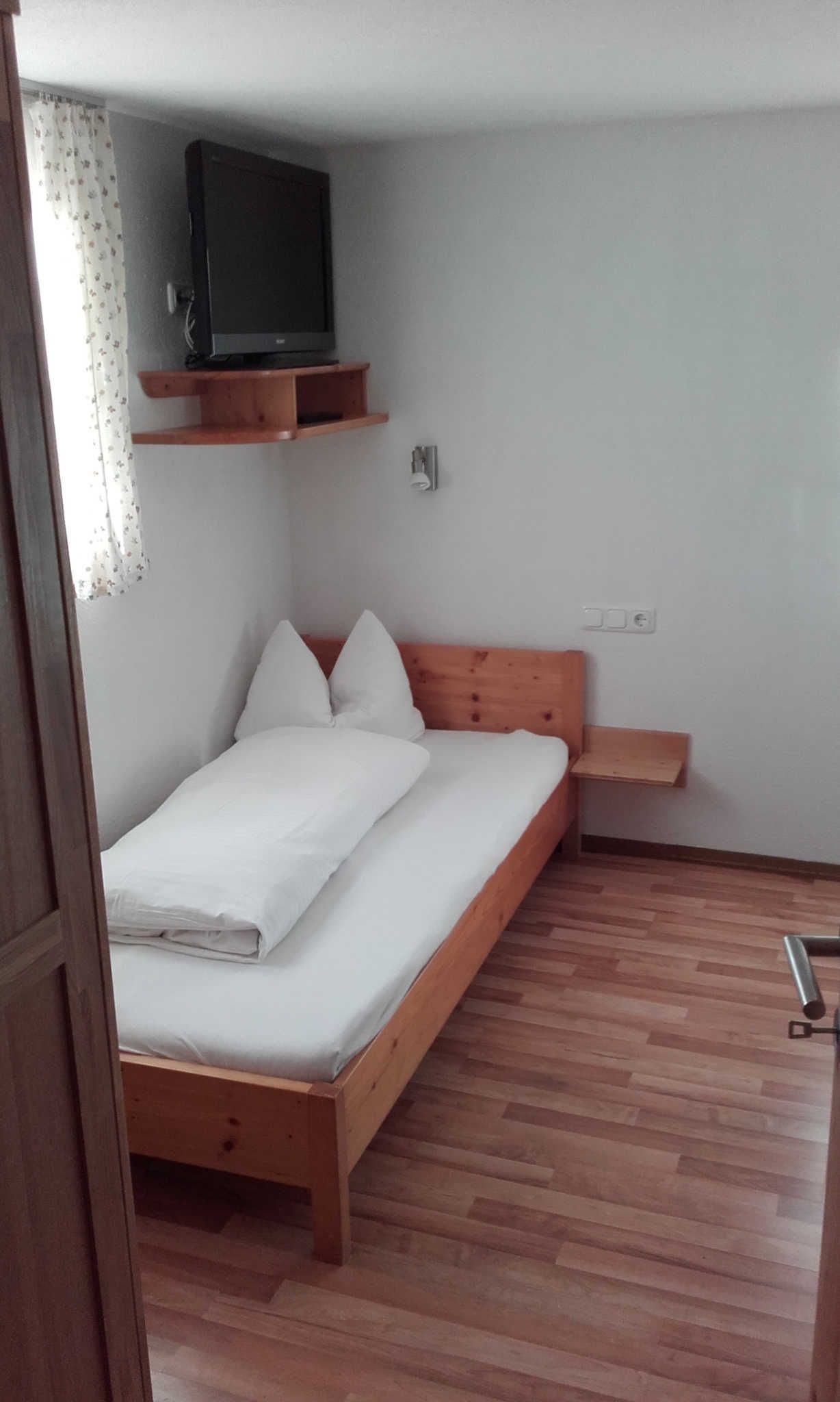 Een slaapkamer met een houten bed, een televisie op een plank en een houten vloer.