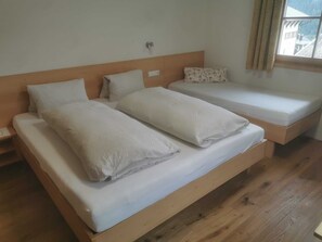 A double bed with a wooden headboard, a single bed with a floral pillow, and a window with curtains.