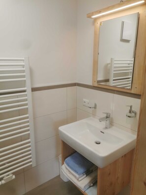 Un baño con lavamanos blanco, espejo, toallero y radiador.