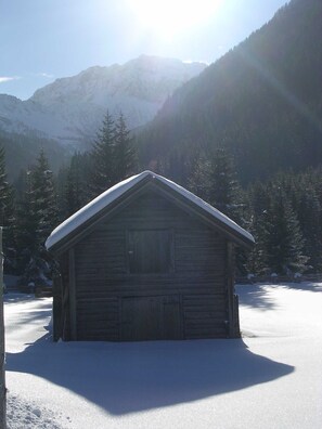 Une cabane en bois, dont le toit est recouvert de neige, entourée d’une forêt et de montagnes.