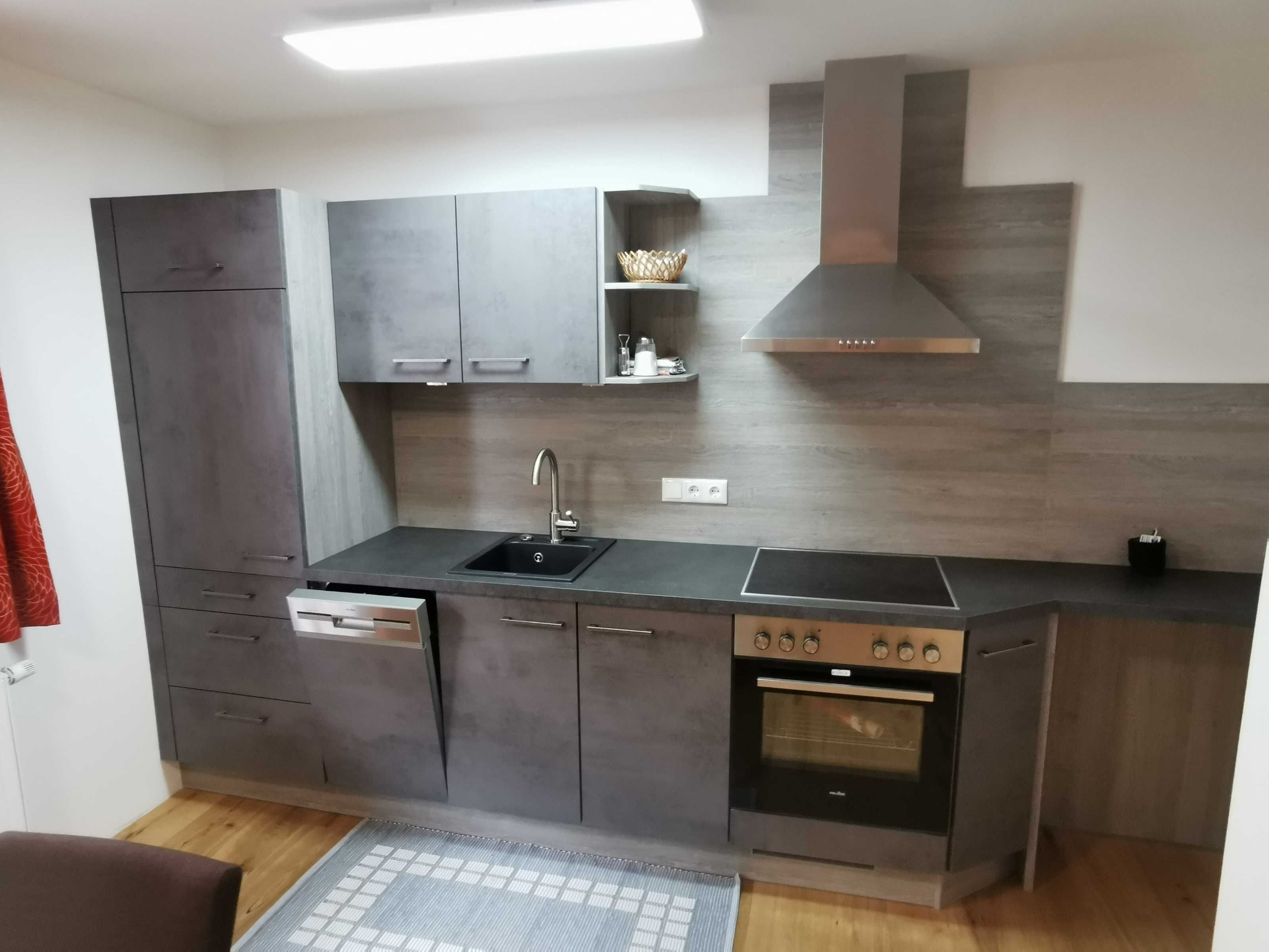 Una cocina moderna con armarios grises, horno integrado, pileta y campana extractora.