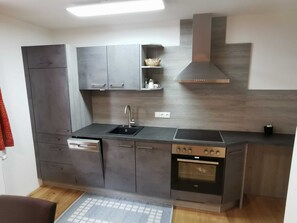 Une cuisine moderne avec des meubles gris, un four encastré, un évier et une hotte aspirante.