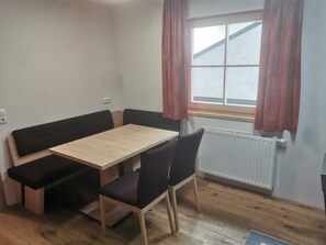 A room with a wooden table, black upholstered benches, and a window with patterned curtains.