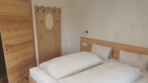 A wooden bed with two pillows, a wooden door with a circular window, and a light switch on the wall.