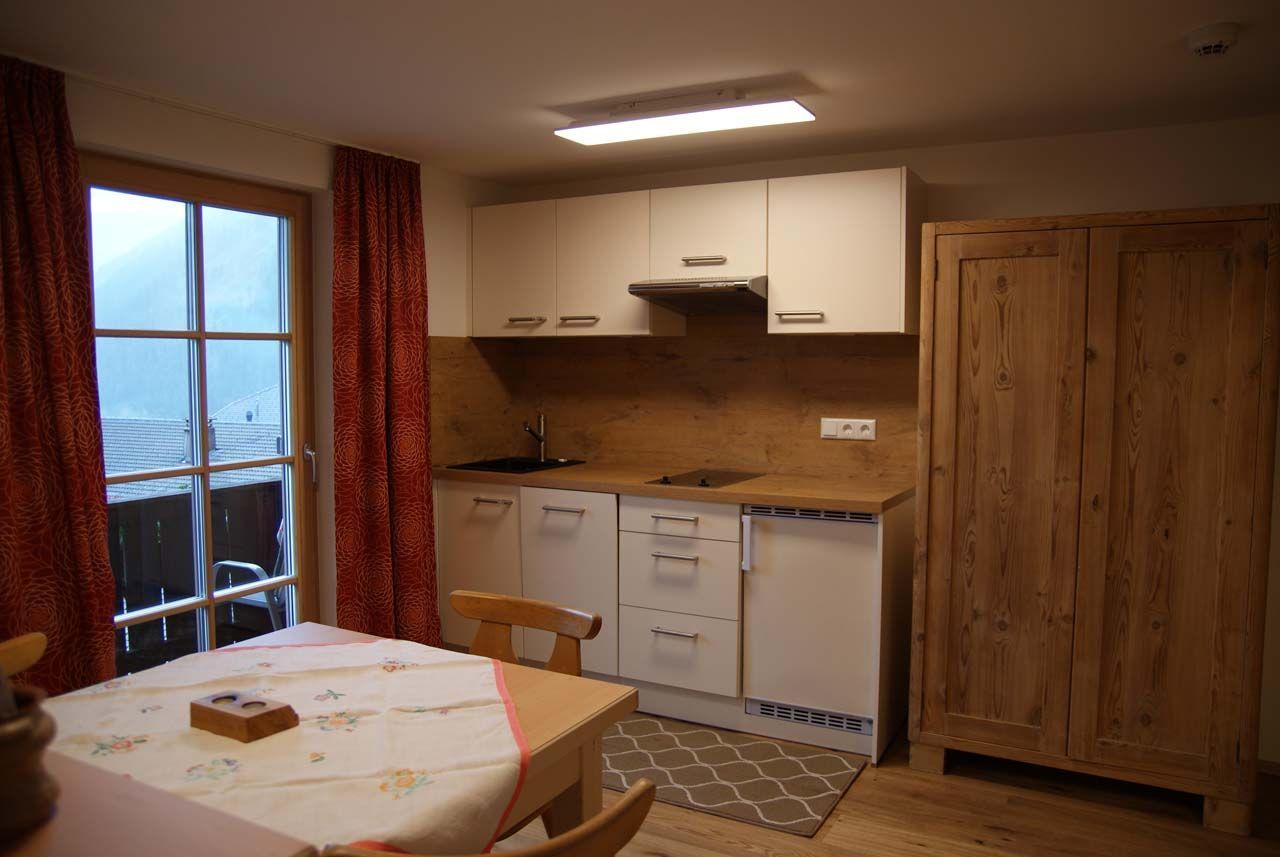 Una cocina compacta con armarios blancos, encimera de madera, estufa integrada y una ventana con cortinas rojas.