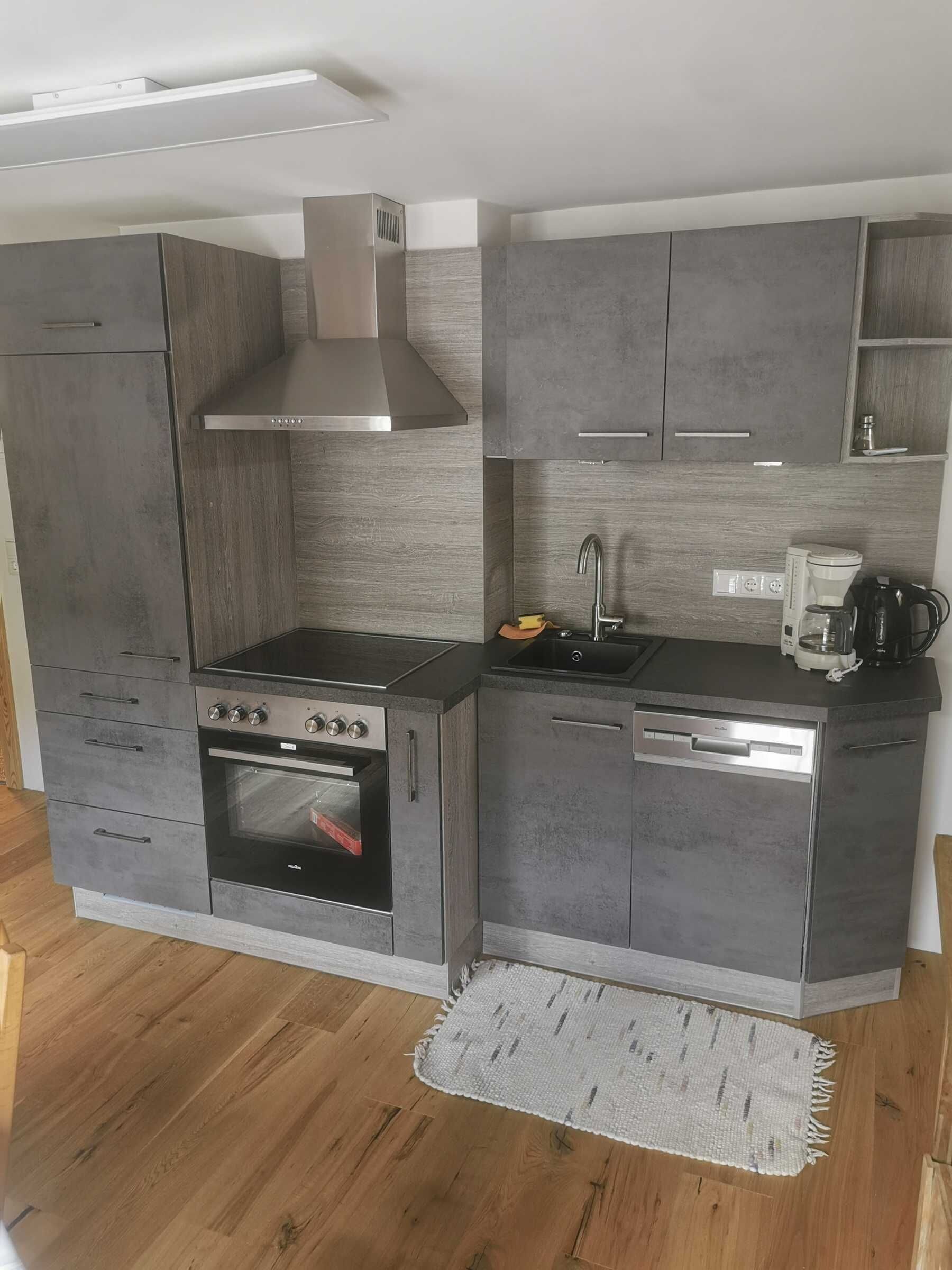 A compact kitchen with a built-in oven, a stovetop, a sink, and a coffee maker.