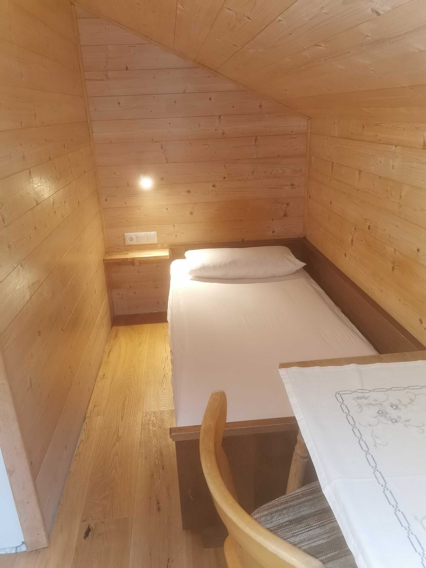 Ein kleines Zimmer im Chalet-Stil mit einem Bett, einem Sessel und einem Tisch.