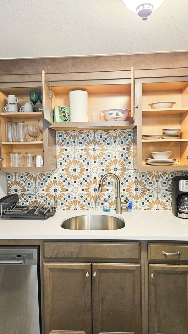 A kitchen with a stainless steel sink, wooden cabinets, and a patterned backsplash.