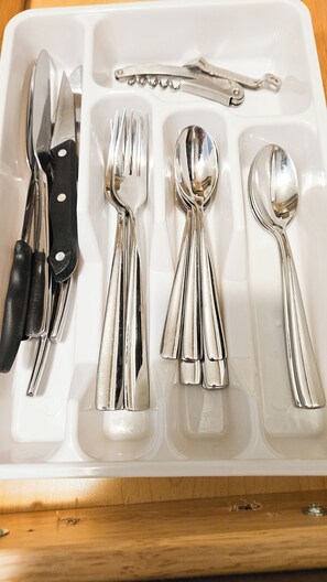 A white tray with cutlery including a knife, fork, spoon, and a pair of tongs.