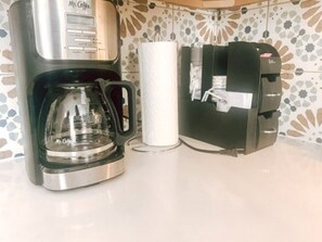 A coffee maker, a paper towel dispenser, and a coffee machine on a kitchen counter.