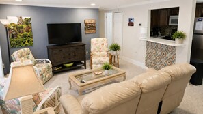 Ein Wohnzimmer mit Sofa, Sessel, Couchtisch, Fernseher und einer Küchenzeile inklusive Mikrowelle und Kühlschrank.