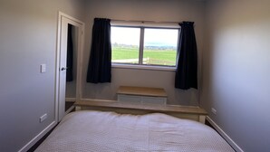 Ein Schlafzimmer mit einem Einzelbett, einem Fenster mit Vorhängen, einem Nachttisch und Blick auf ein grünes Feld.
