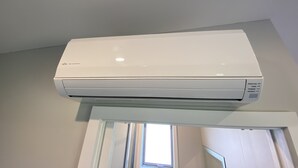 Eine weiße Klimaanlage ist an einer Zimmerdecke montiert, im Raum befinden sich ein Fenster und eine Tür.