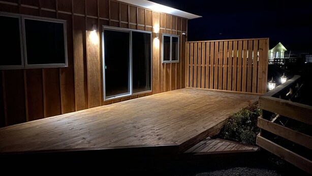 Eine Holzterrasse mit einer Rampe zu einer Schiebetür, umgeben von einem Holzzaun und einem kleinen Garten.