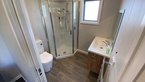 Ein Badezimmer mit Glasdusche, Toilette, Waschbecken und Spiegel sowie einem Fenster.