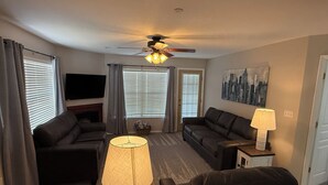 Un salon avec un ventilateur de plafond, deux canapés, un téléviseur et un tableau accroché au mur.