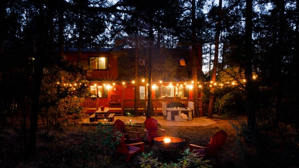 Eine rustikale Holzhütte mit Feuerstelle und Sitzbereich im Freien, umgeben von Bäumen.