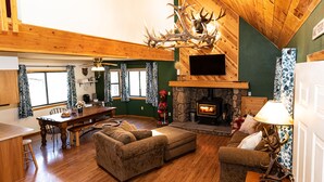 Ein gemütliches Wohnzimmer mit Kamin aus Stein, Holzboden und einem großen Kronleuchter aus Geweihen.