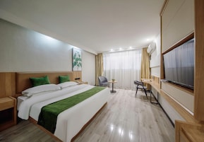 Una habitación de hotel con cama, escritorio, silla, televisor y ventana con cortinas.