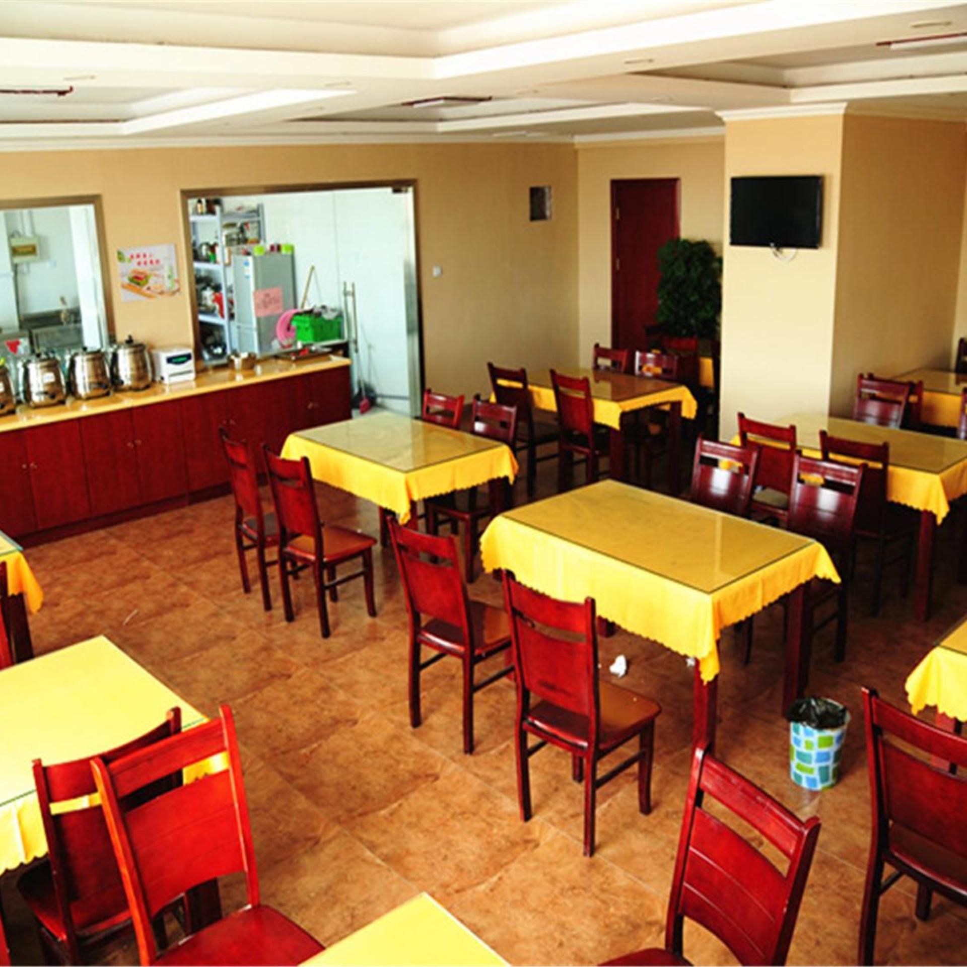 A dining area with multiple tables and chairs, a kitchen area with utensils and appliances, and a television mounted on the wall.