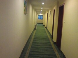 Un pasillo de hotel con pisos alfombrados, puertas a ambos lados y una ventana al final.