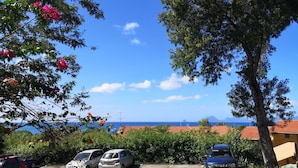 A parking area with several cars, trees, and a view of the sea and distant mountains.