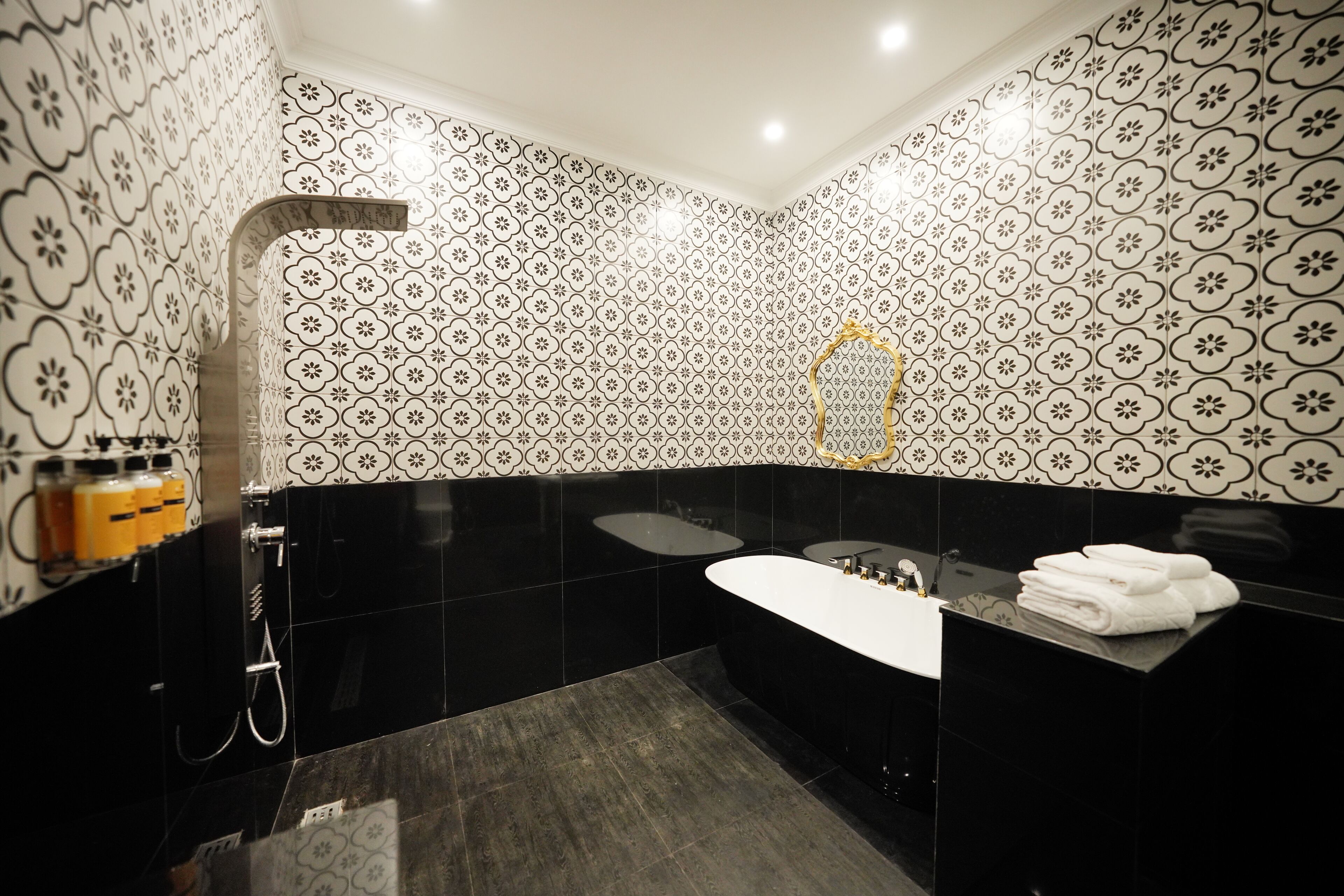 A modern bathroom with black and white patterned tiles, a freestanding bathtub, a vanity with a mirror, and a towel rack.