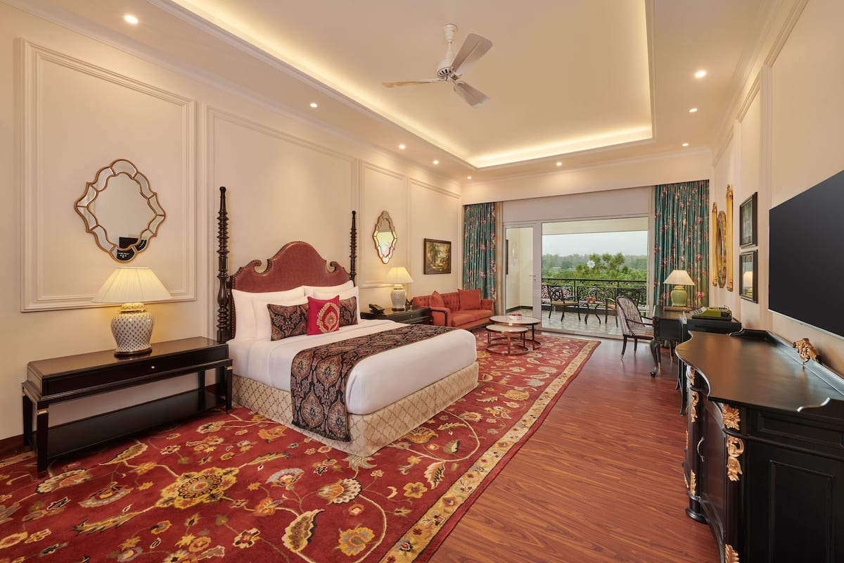 A spacious hotel room with a large bed, a sitting area with a view, and a balcony.