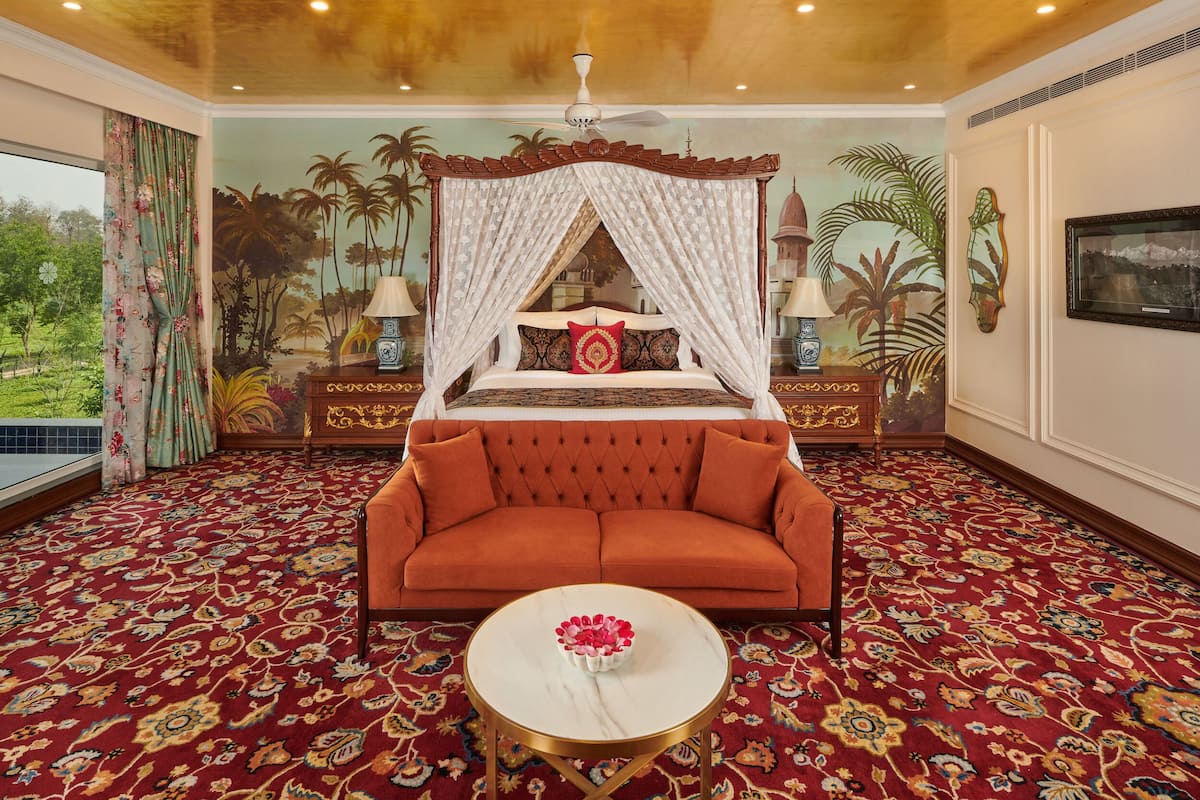 A bedroom with a four-poster bed, a red sofa, a round coffee table, and a mural of palm trees on the wall.