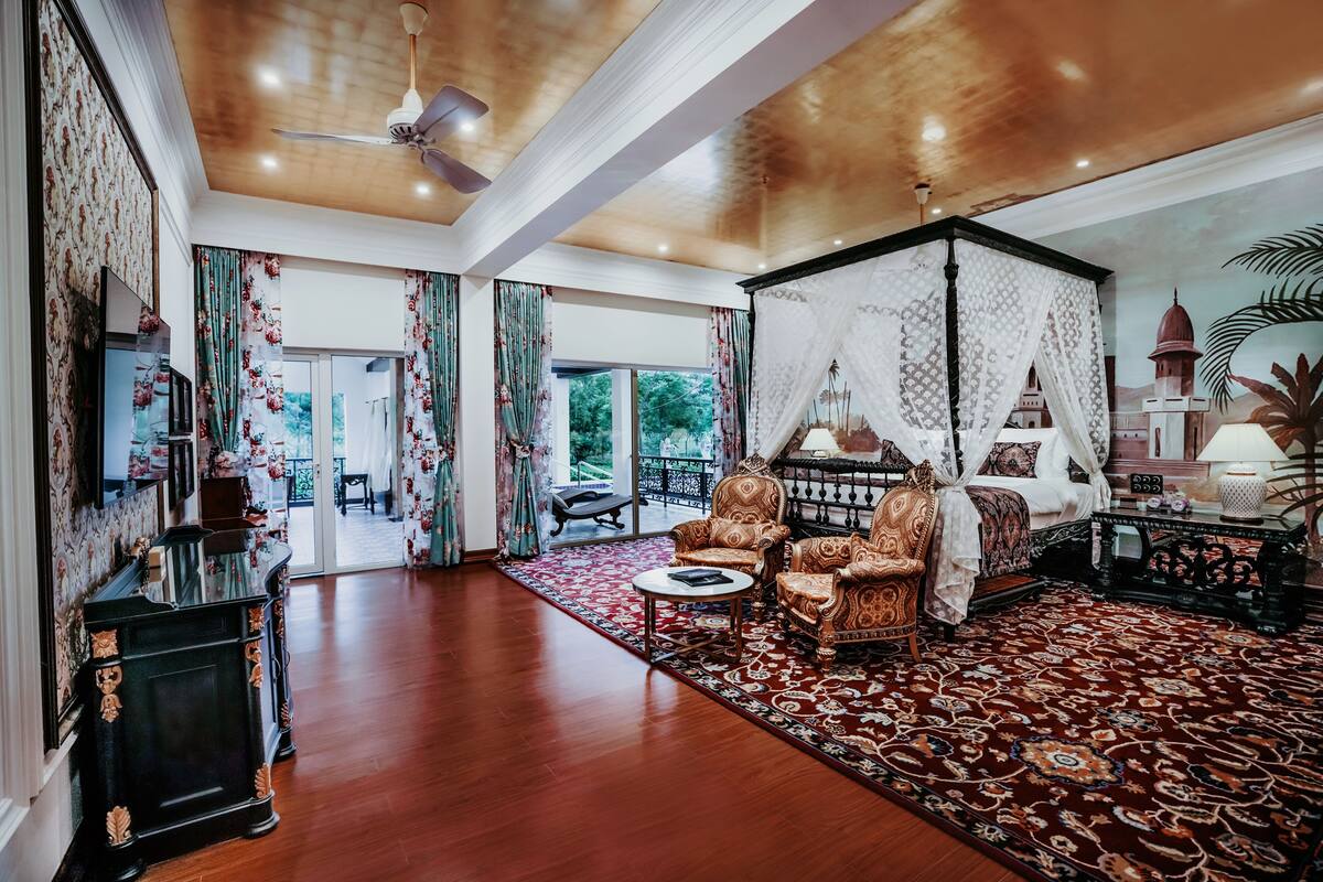 A spacious living room with a large wooden ceiling, a four-poster bed, and a view of the outdoors through large windows.