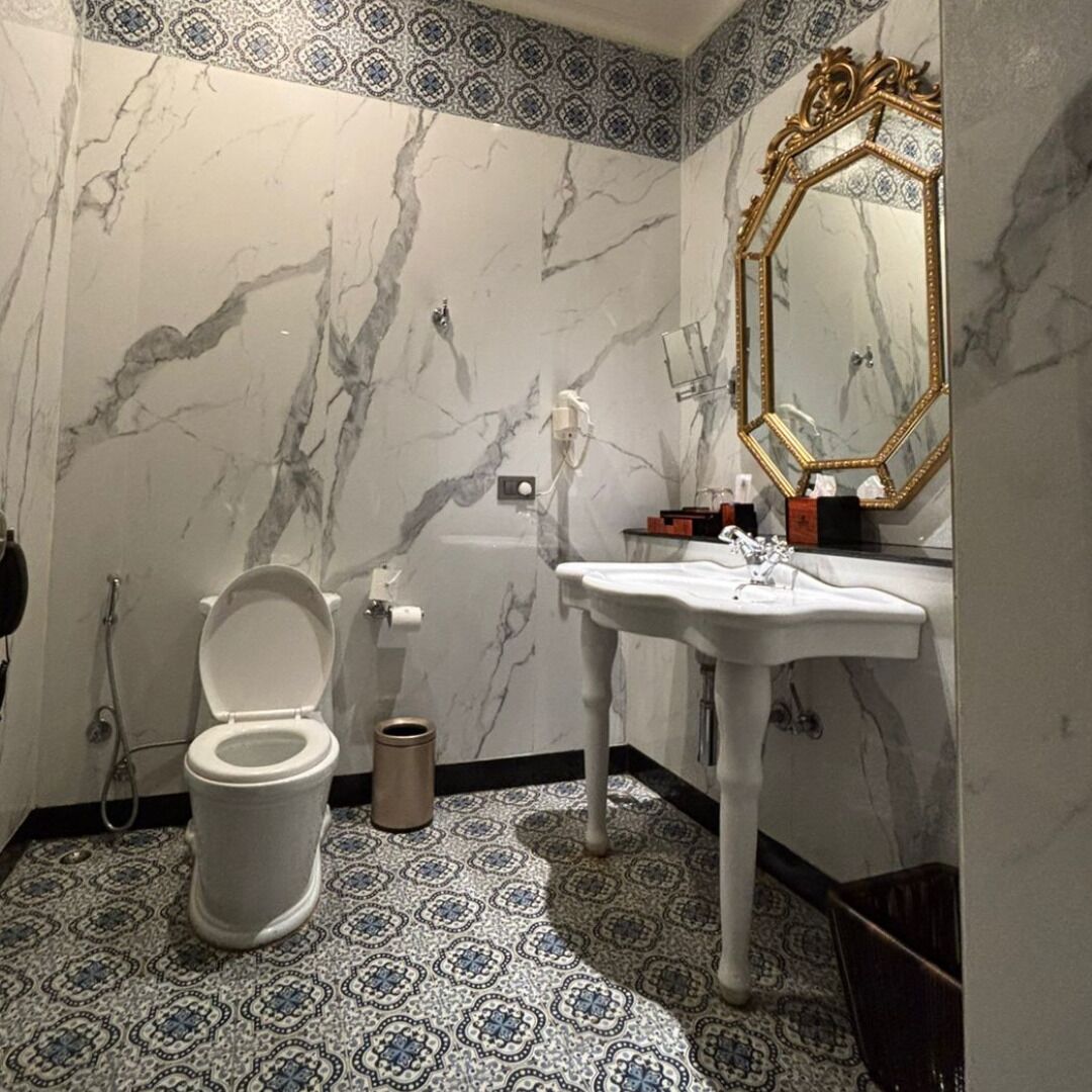 A bathroom with a toilet, sink, and mirror. The walls have a marble pattern, and the floor has a patterned tile design.