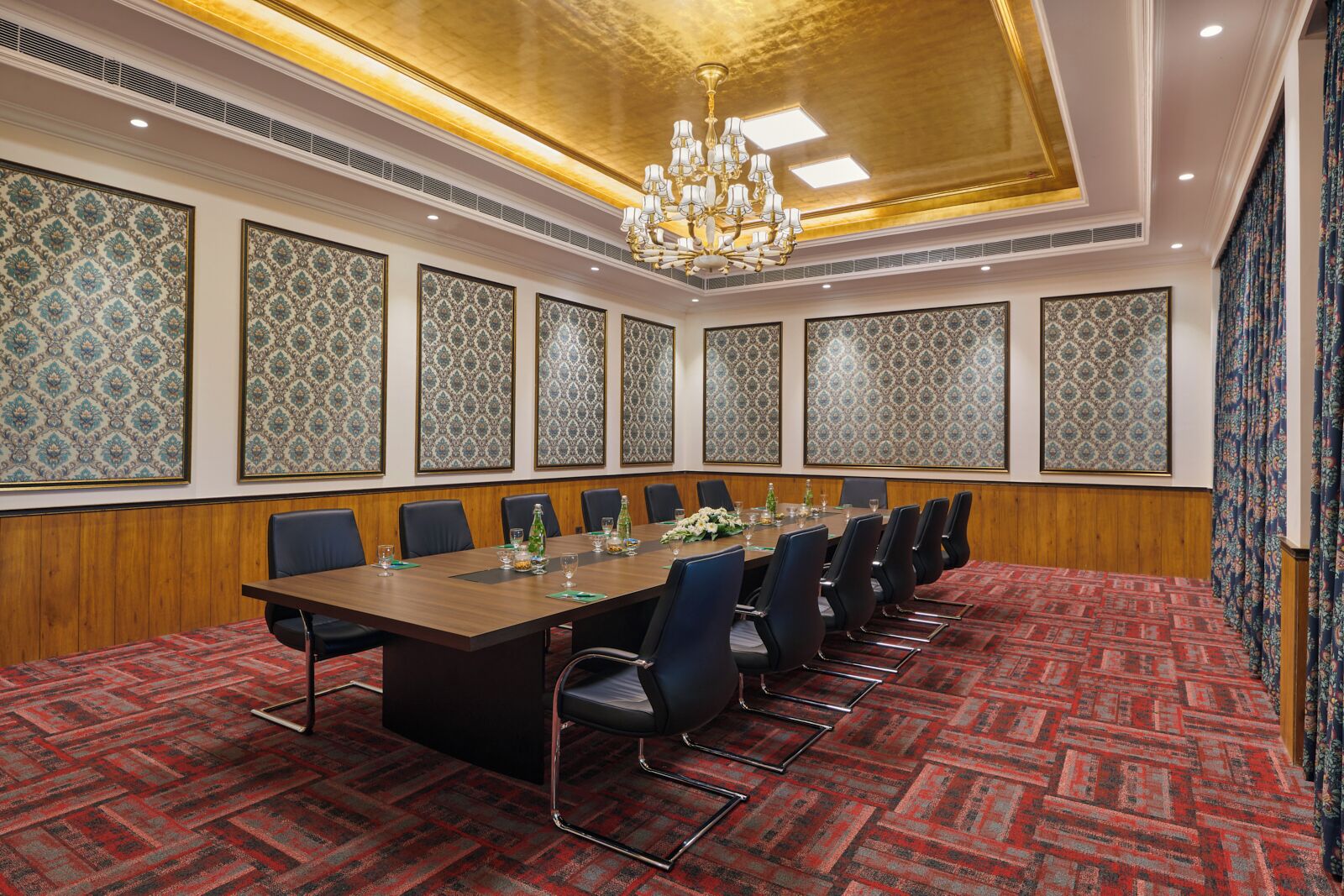 A conference room with a long table, chairs, patterned wallpaper, and a chandelier.