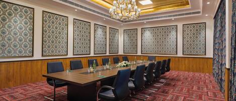 A conference room with a long table, chairs, patterned wallpaper, and a chandelier.