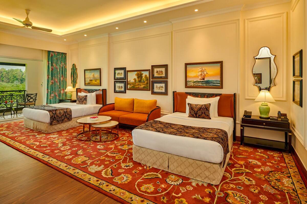 A hotel room with two beds, a sofa, a small table, and a balcony with a view.